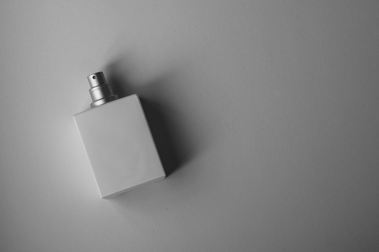 gallery-1 A sleek white perfume bottle photographed on a gray background with soft, muted lighting.